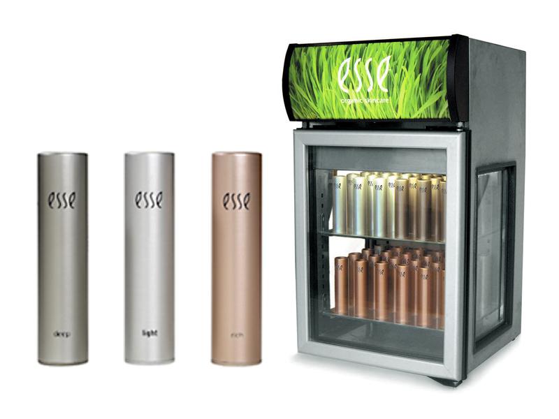 Three metallic canisters labeled "esse" in silver, light gold, and bronze shades stand next to a refrigerator displaying similar canisters inside. The fridge sign reads "esse" with a grass background.